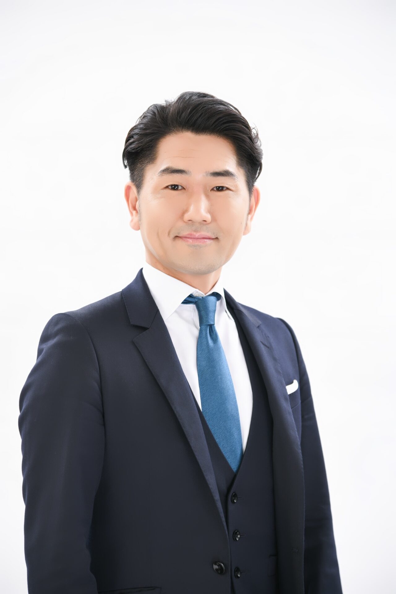 Professional head-and-shoulders portrait of a smiling Asian man in a dark navy suit and blue tie against a white background.